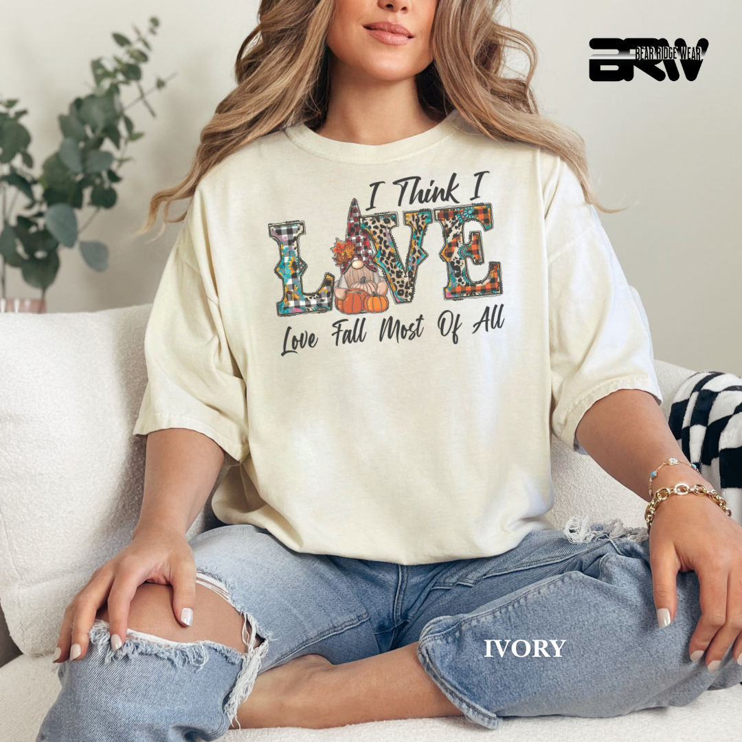 Person wearing a IVORY sweatshirt with colorful text design sitting on a couch. I THINK I LOVE FALL THE MOST