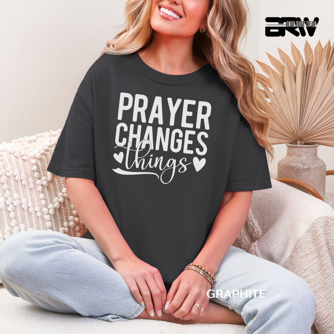 Person wearing a black t-shirt with 'PRAYER CHANGES THINGS' text, sitting on a couch.