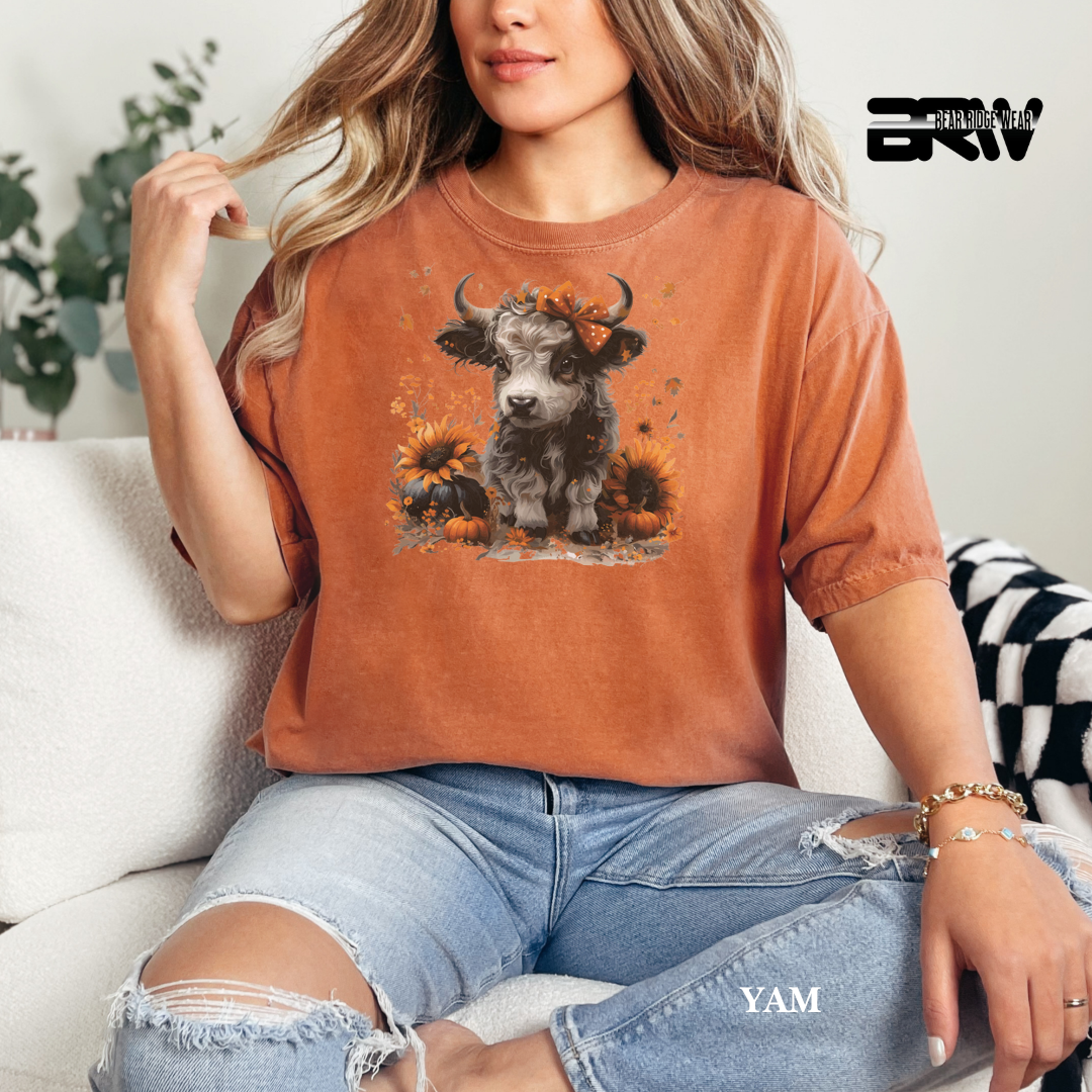 Person wearing a brown t-shirt with a cow and sunflower design, sitting on a couch.