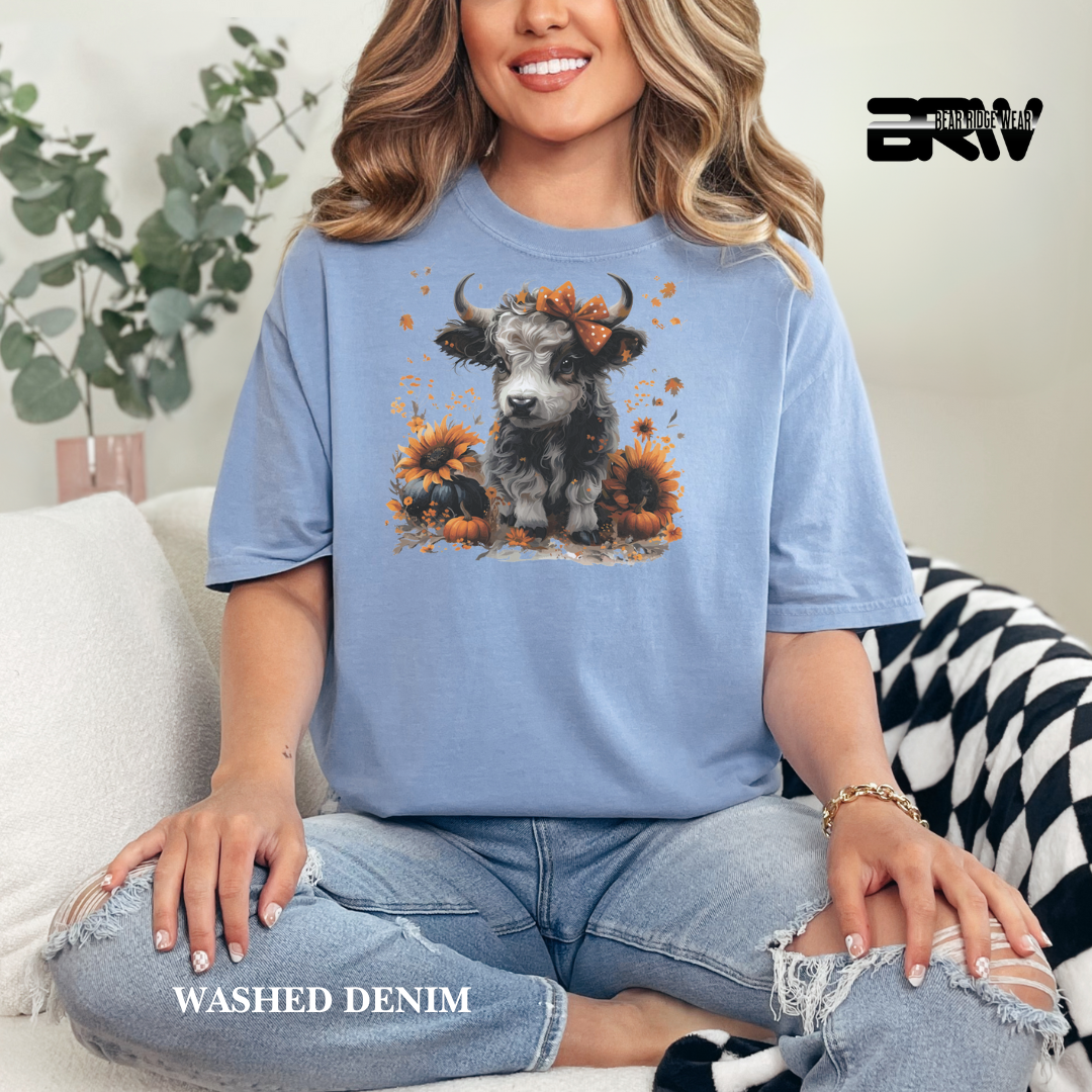 Woman wearing a blue t-shirt with a cow and sunflower design, sitting on a couch.