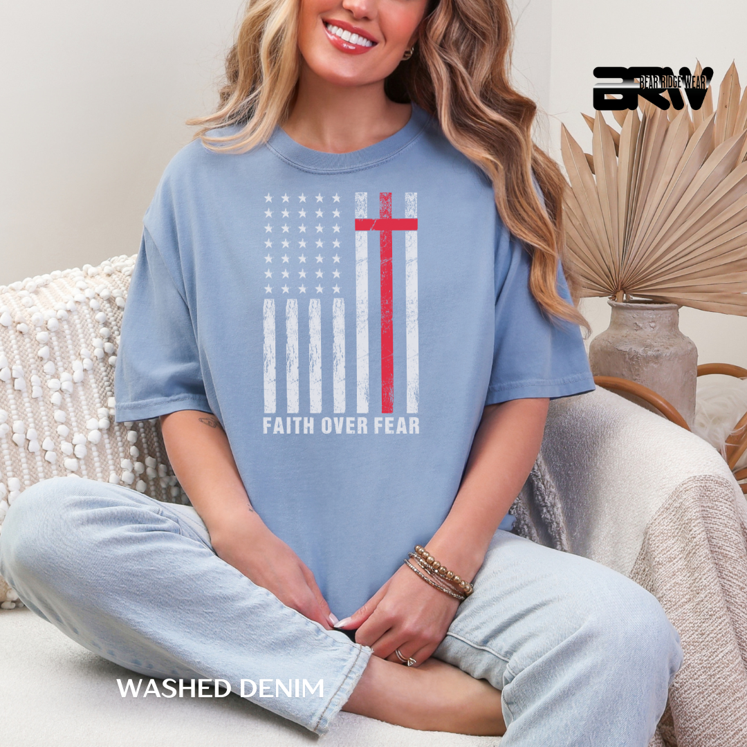 Woman wearing a blue t-shirt with an American flag design and 'Faith Over Fear' text, sitting on a couch.