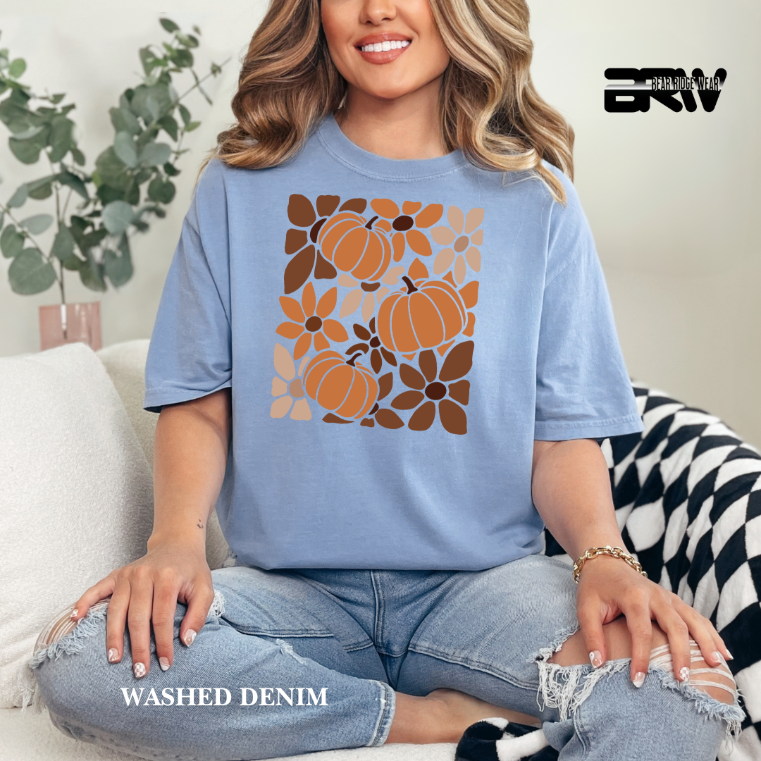 Woman wearing a blue t-shirt with pumpkin and flower design, sitting on a couch.