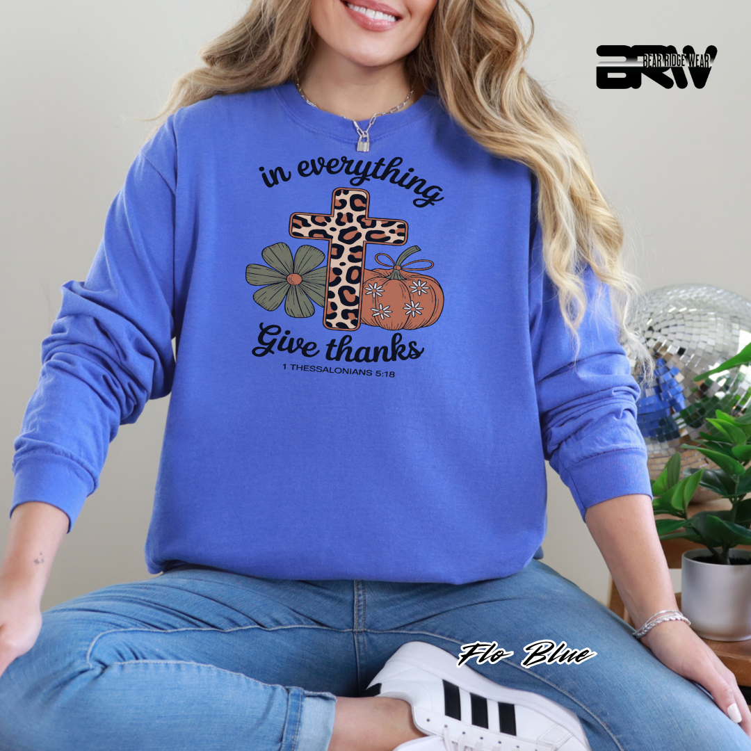 Person wearing a blue sweatshirt with a cross, flowers, and pumpkins design, sitting on a chair.
