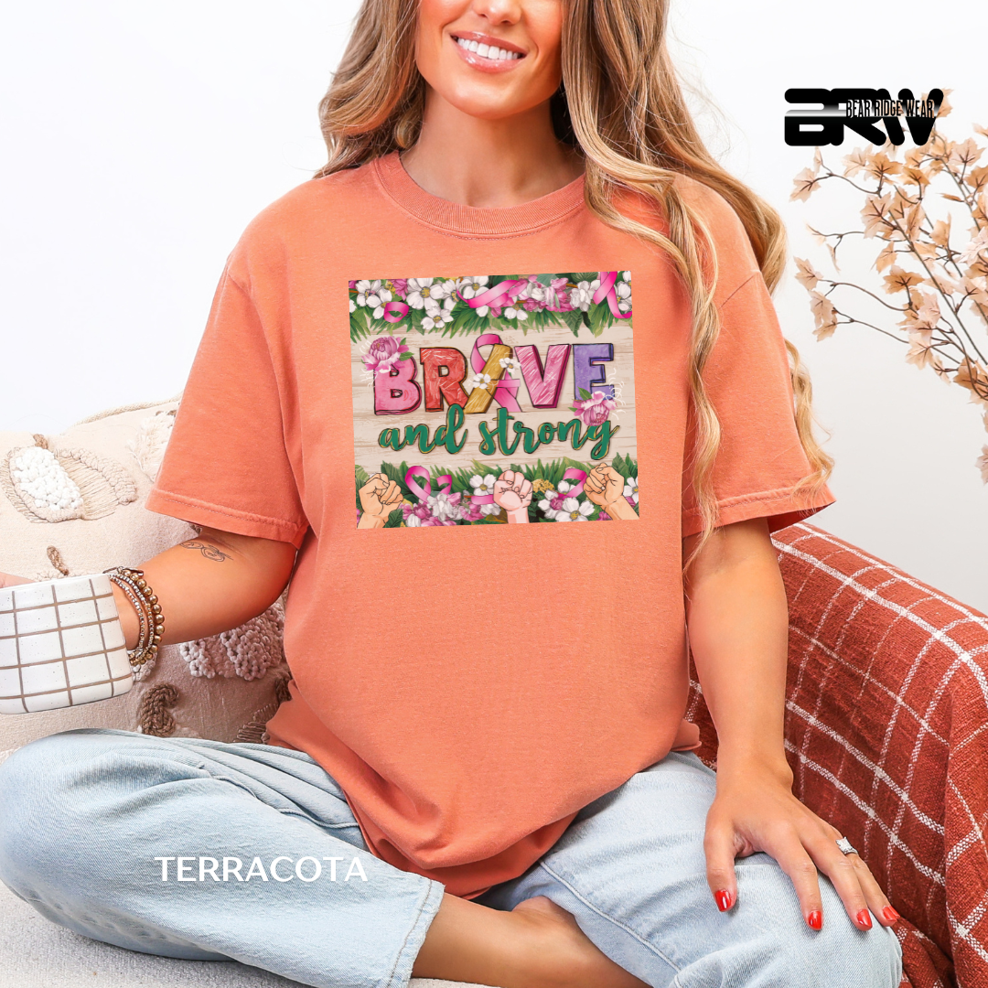 Woman wearing a terracotta-colored t-shirt with 'Brave and Strong' design, sitting on a couch.