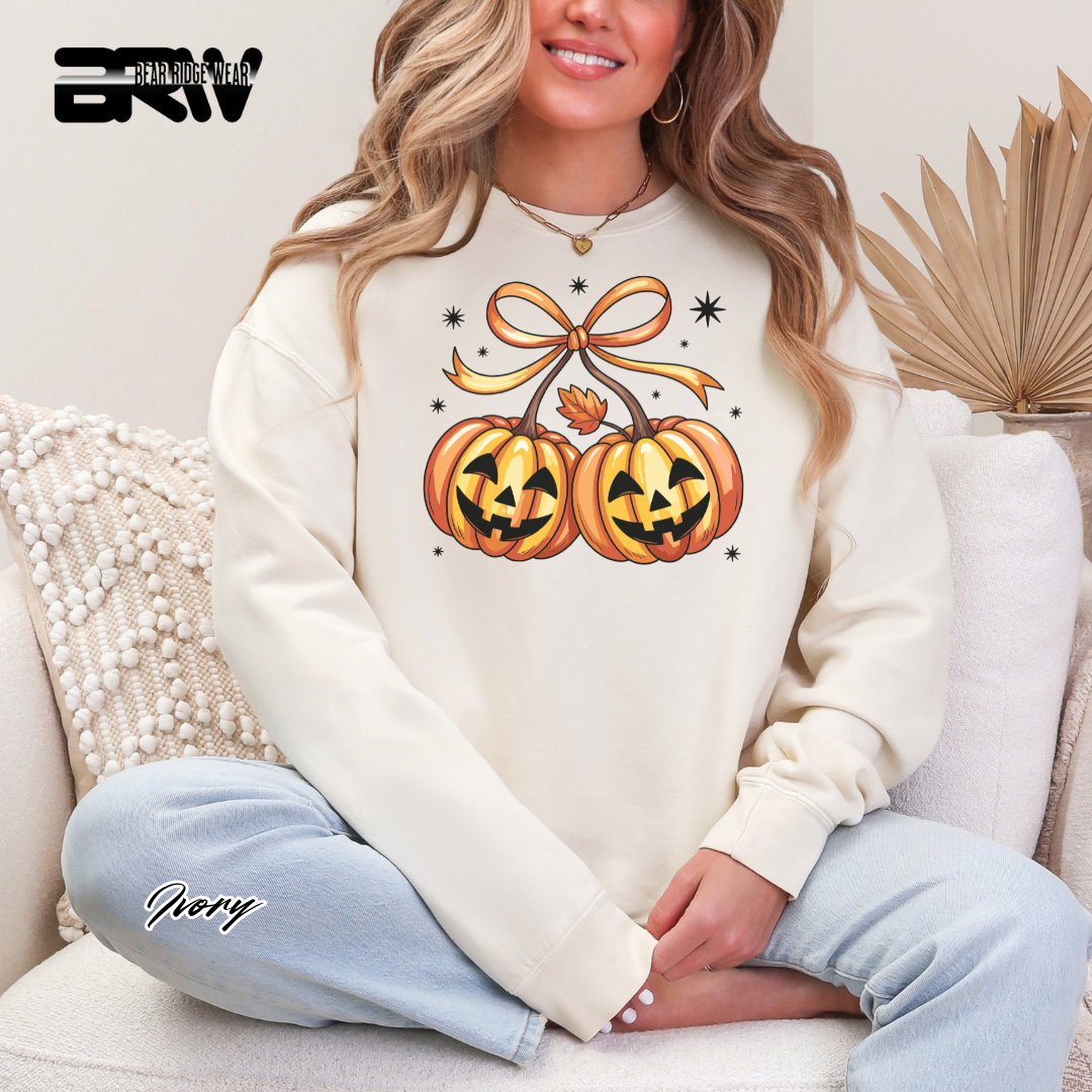 Woman wearing a white sweatshirt with Halloween-themed design sitting on a couch. PUMPKIN CHERRIES HALLOWEN SWEATSHIRT