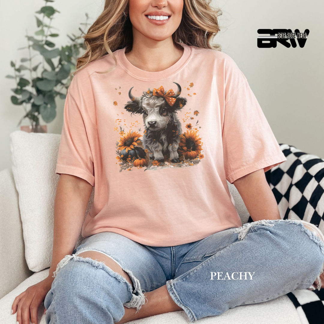 Person wearing a peach t-shirt with a cow and sunflower design, sitting on a couch.