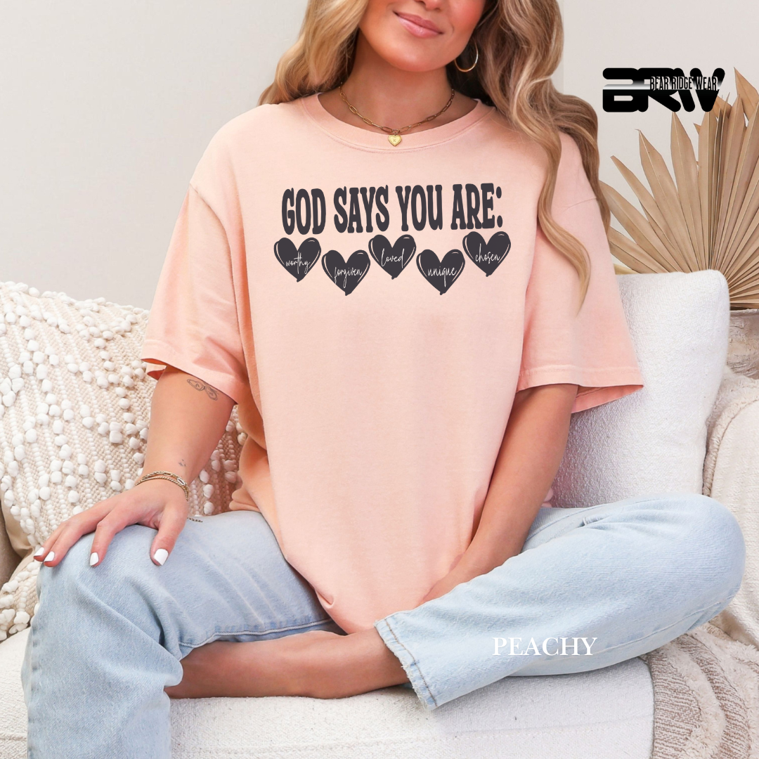 Person wearing a peach t-shirt with text sitting on a couch. FAITH TEE