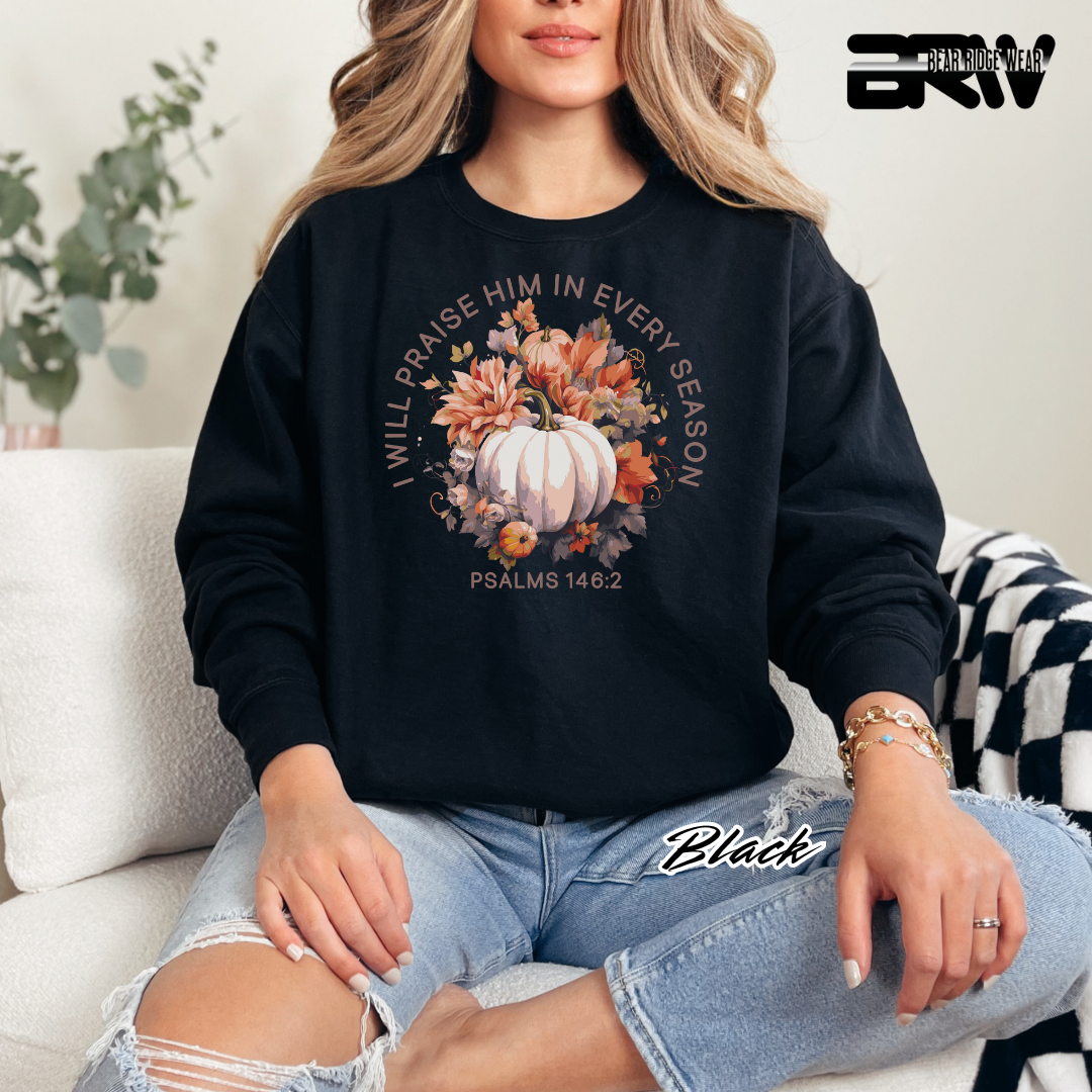 Person wearing a black sweatshirt with a pumpkin and floral design, sitting on a couch.