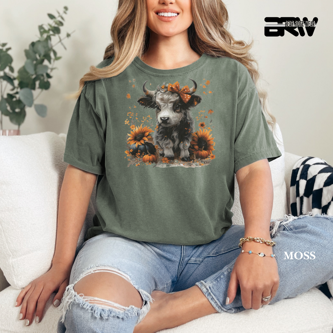 Woman wearing a green t-shirt with a cow and sunflower design, sitting on a couch.