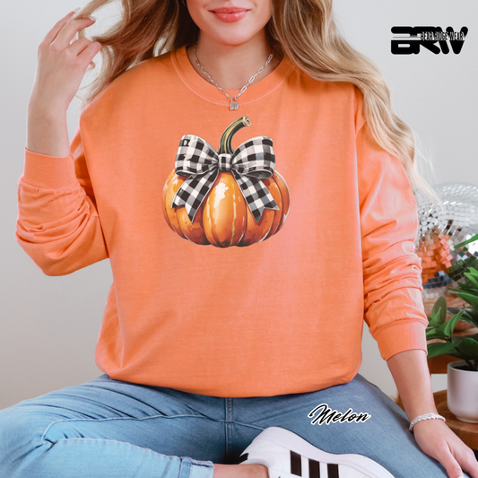 Person wearing an orange sweatshirt with a pumpkin design and plaid bow, sitting indoors.