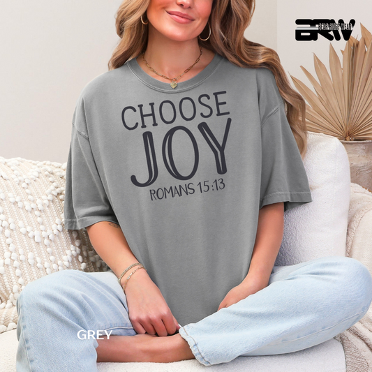 Woman wearing a gray t-shirt with 'CHOOSE JOY ROMANS 15:13' text, sitting on a couch.