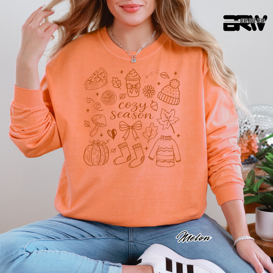 Person wearing an orange sweatshirt with 'cozy season' design, sitting indoors.