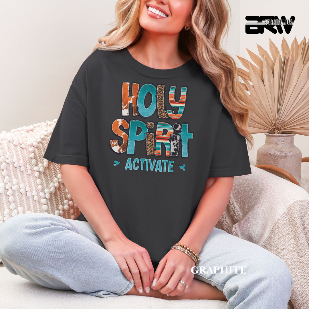 Person wearing a black t-shirt with colorful text 'Holy Spirit Activate' sitting on a couch.