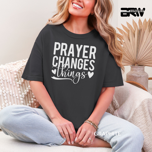 Person wearing a black t-shirt with 'PRAYER CHANGES THINGS' text, sitting on a couch.