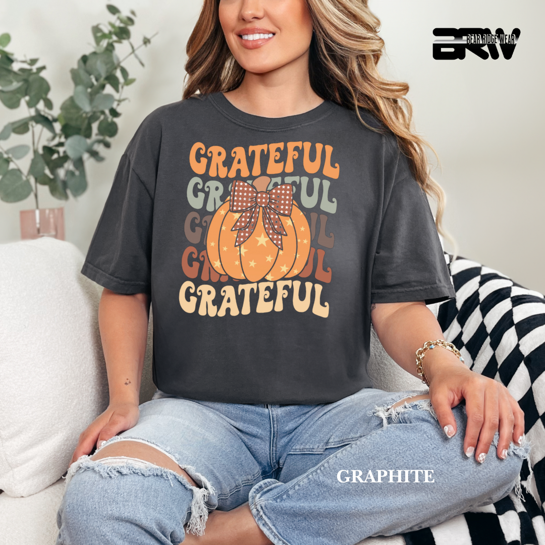 Person wearing a dark gray t-shirt with 'Grateful' text and pumpkin graphic, sitting on a couch.