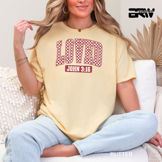 Woman wearing a yellow t-shirt with 'LOVED John 3:16' text, sitting on a couch.