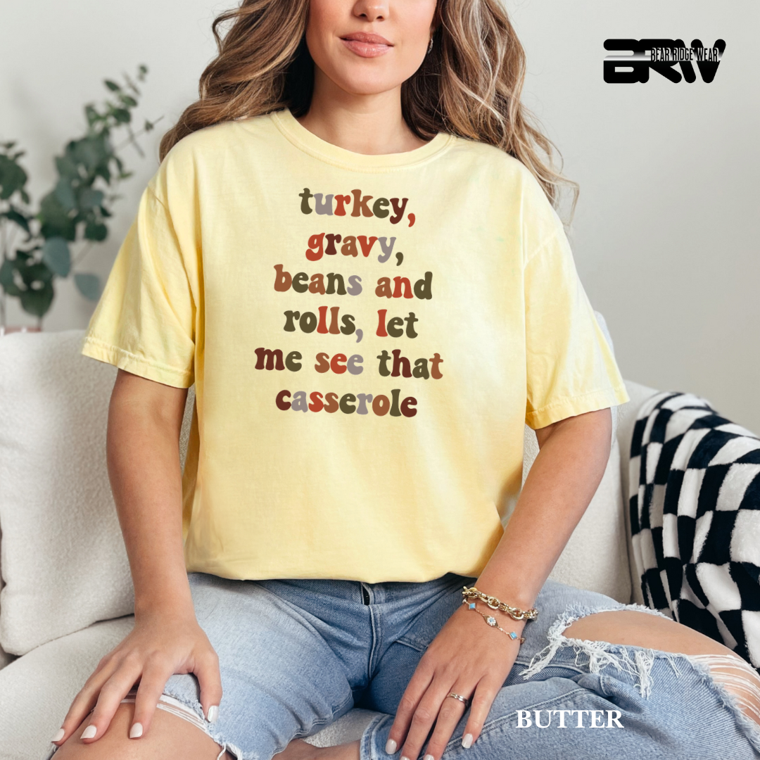 Person wearing a yellow t-shirt with text, sitting on a couch. FALL TEE