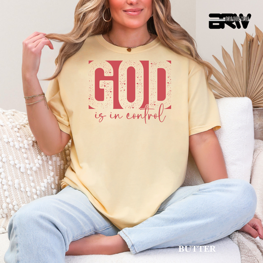 Woman wearing a yellow t-shirt with 'God is in control' text, sitting on a couch.