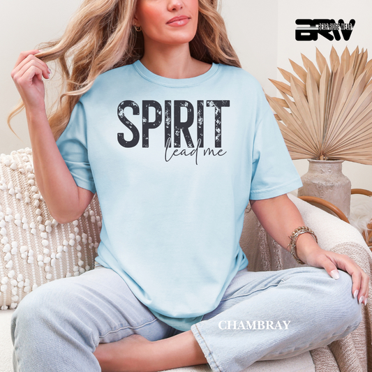 Woman wearing a light blue t-shirt with 'SPIRIT lead me' text, sitting in a cozy room.