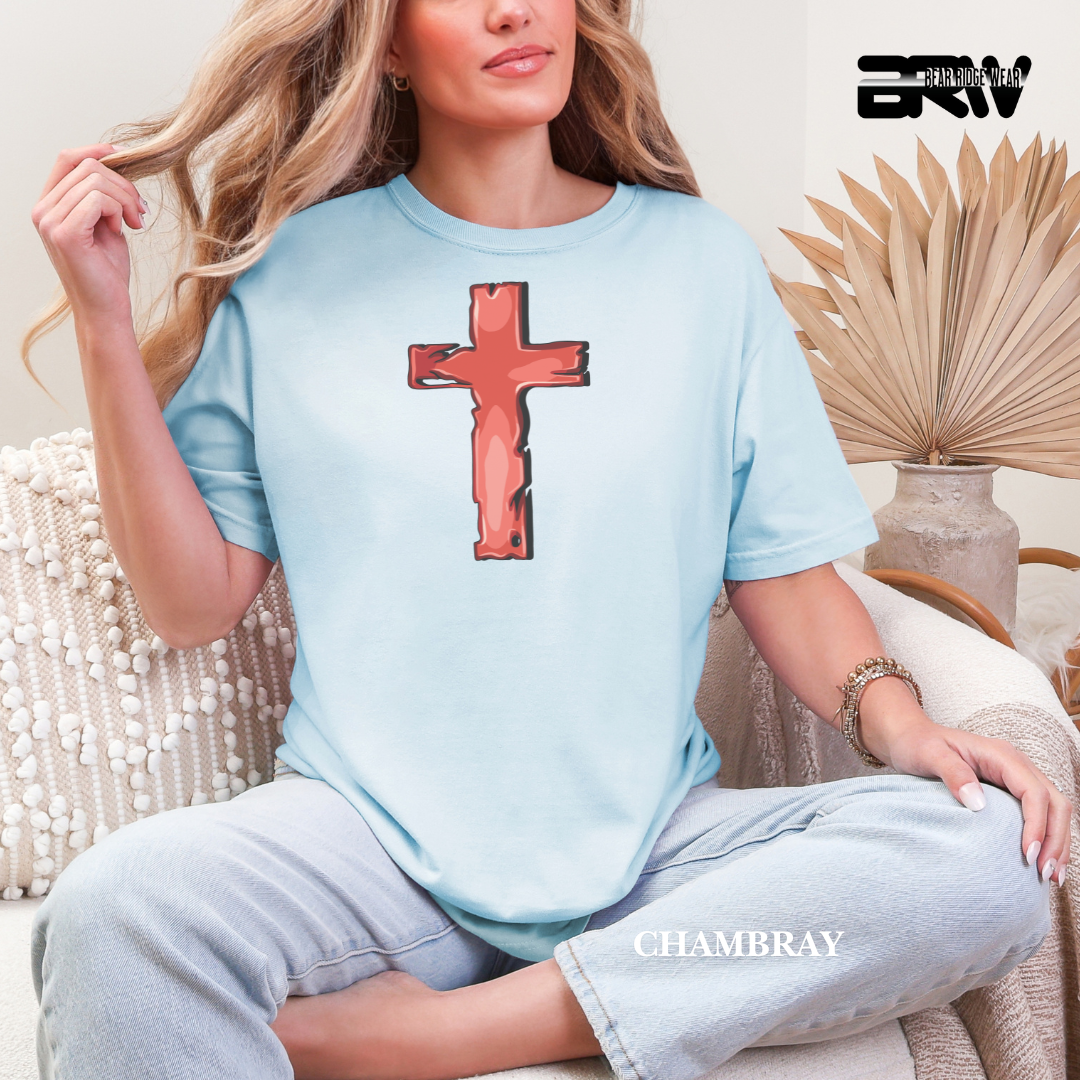 Woman wearing a light blue t-shirt with a red cross design, sitting in a casual setting.