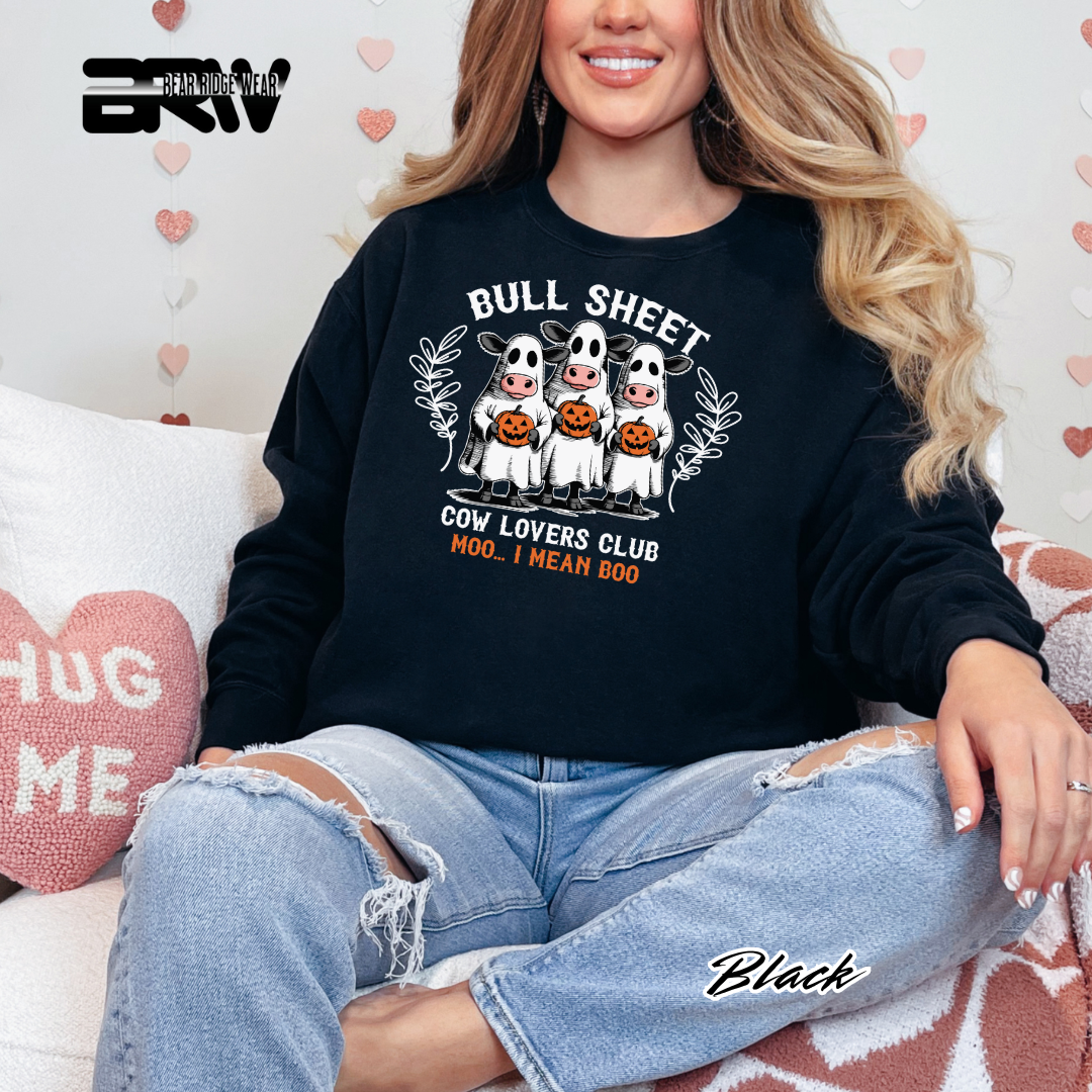 Person wearing a black sweatshirt with a graphic design, sitting on a couch with a heart-patterned background.
