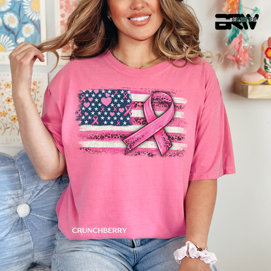 Woman wearing a pink t-shirt with a breast cancer awareness ribbon design, sitting on a couch.
