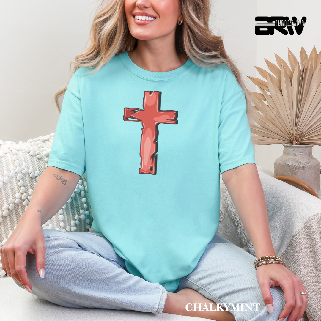Woman wearing a light blue t-shirt with a red cross design, sitting on a couch.