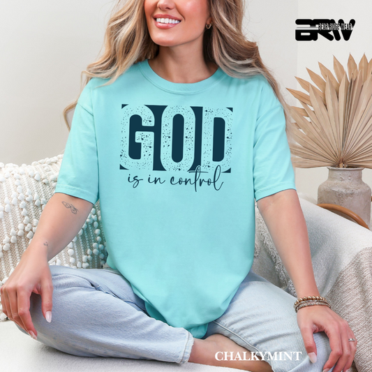Woman wearing a light blue t-shirt with 'God is in control' text, sitting on a couch.
