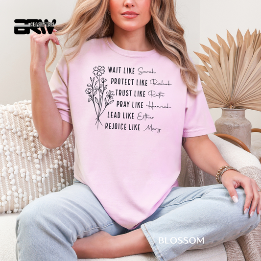 Person wearing a pink t-shirt with text and floral design, sitting on a couch.