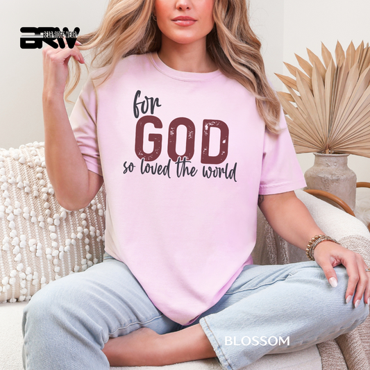 Person wearing a pink t-shirt with text, sitting on a couch. FOR GOD SO LOVE THE WORLD FAITH TEE 