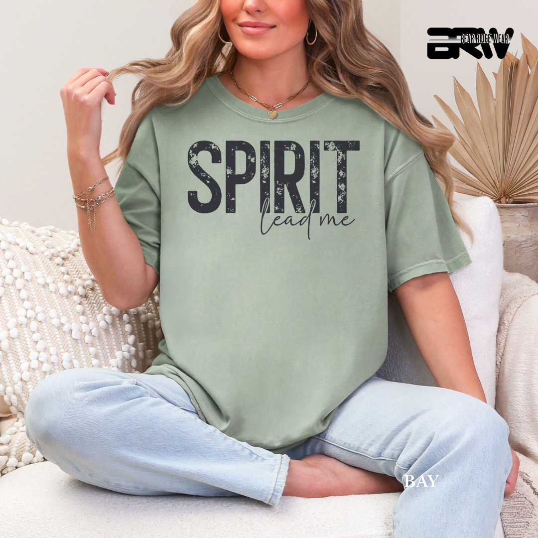 Woman wearing a green t-shirt with 'SPIRIT lead me' text, sitting on a couch.