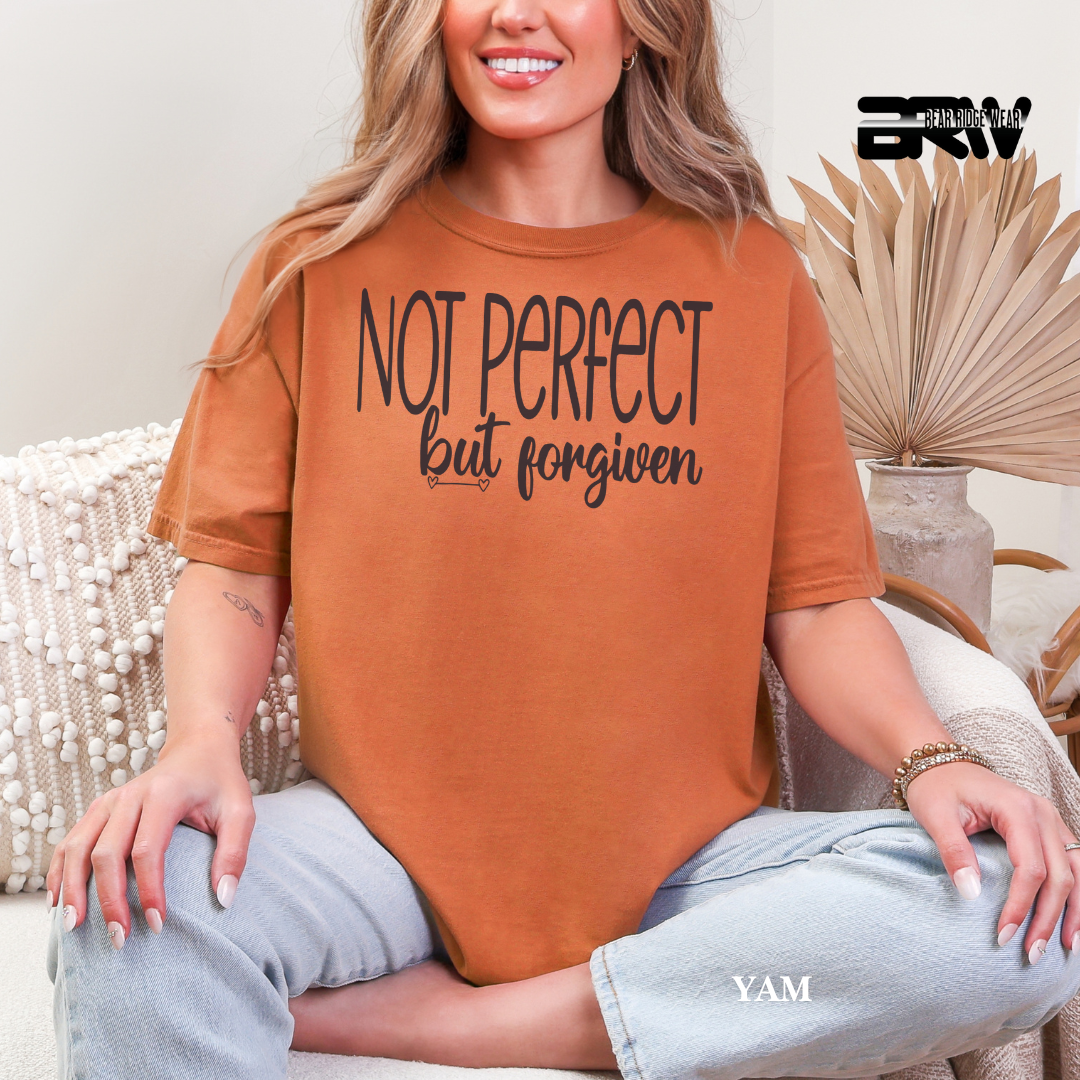 Person wearing a brown t-shirt with 'Not perfect but forgiven' text, sitting on a couch.