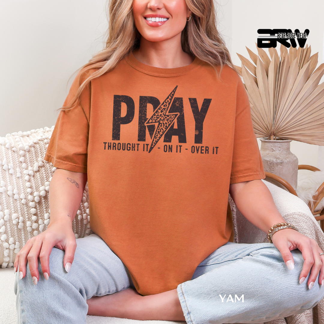 Person wearing a brown t-shirt with 'PRAY THROUGH IT ON IT OVER IT' text, sitting on a couch.