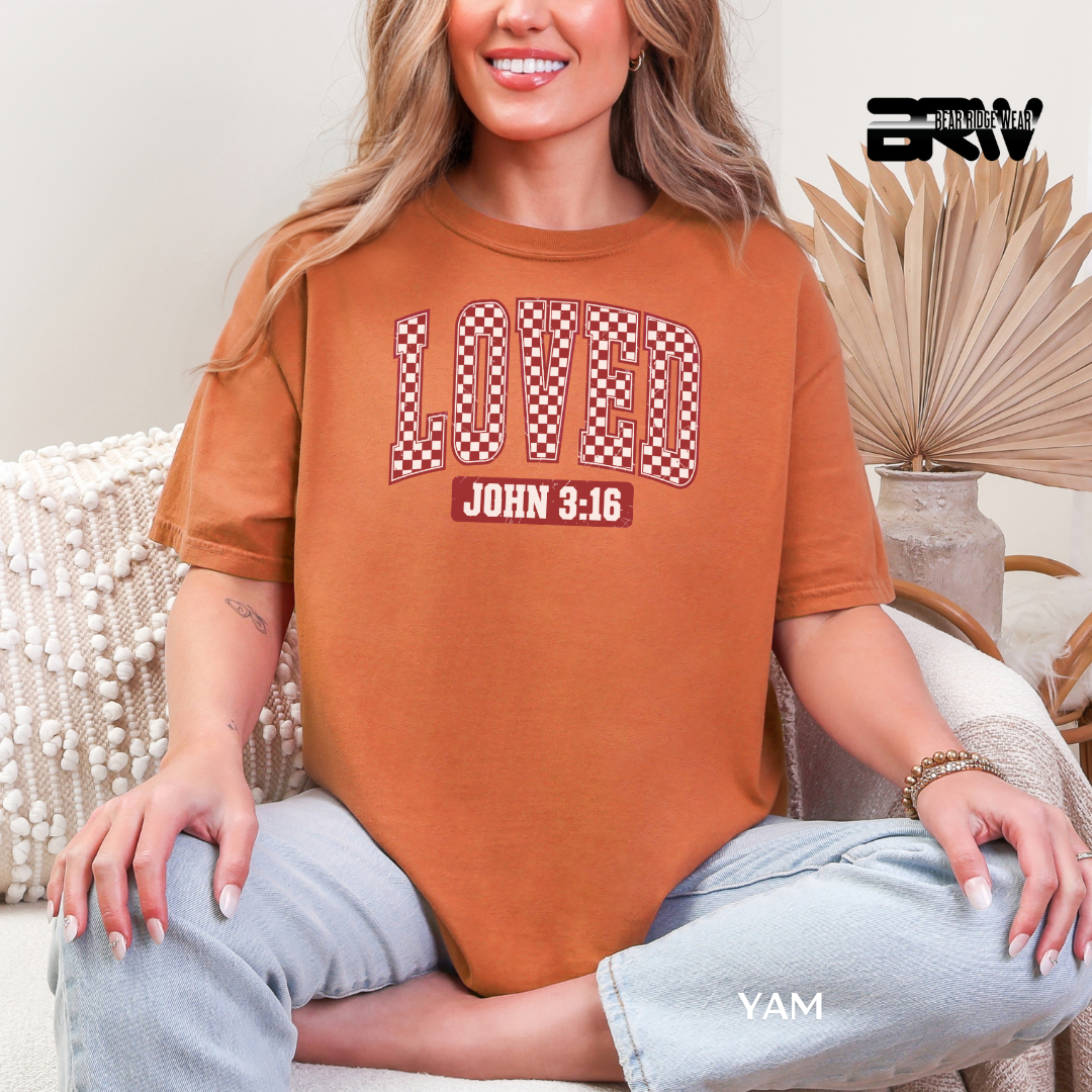 Person wearing a brown t-shirt with 'LOVED John 3:16' text, sitting on a couch.