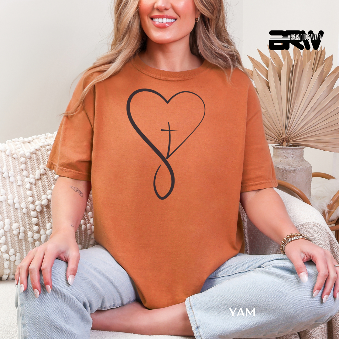 Person wearing a brown t-shirt with a heart and cross design, sitting on a couch.