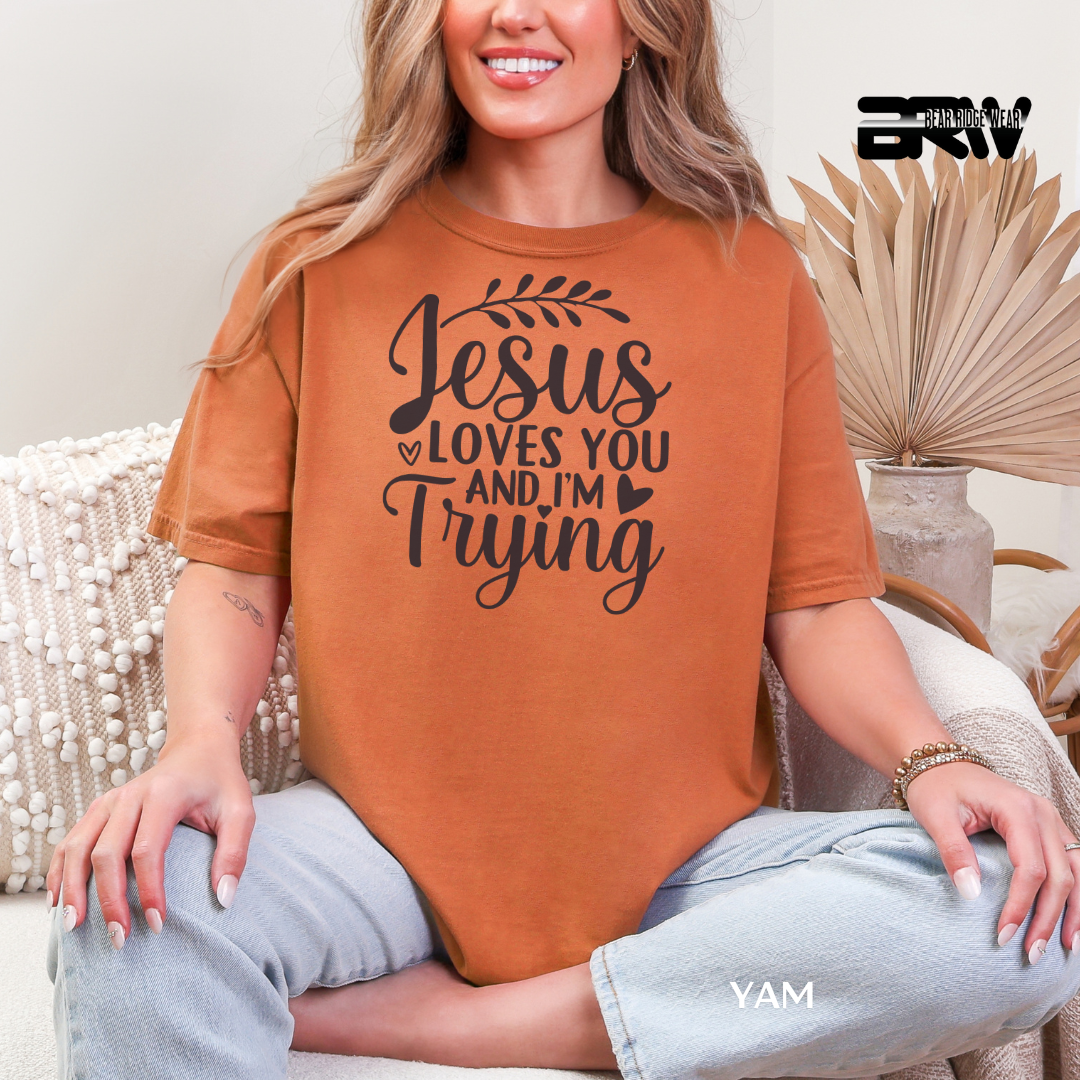 Person wearing a brown t-shirt with 'Jesus loves you and I'm trying' text, sitting on a couch.