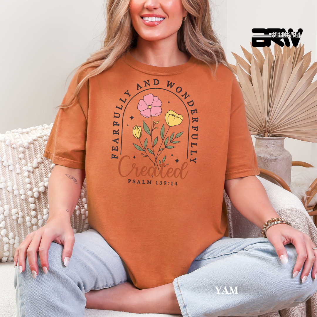 Person wearing a brown t-shirt with floral design and text, sitting on a couch. FAITH TEE 