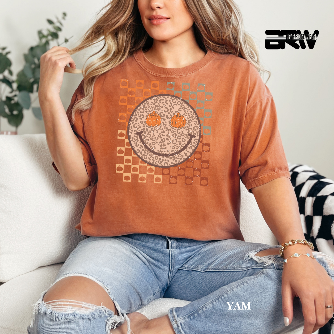 Woman wearing a brown t-shirt with a smiley face design, sitting on a couch.