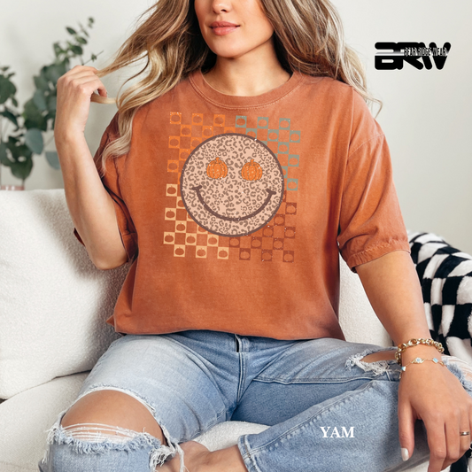 Woman wearing a brown t-shirt with a smiley face design, sitting on a couch.