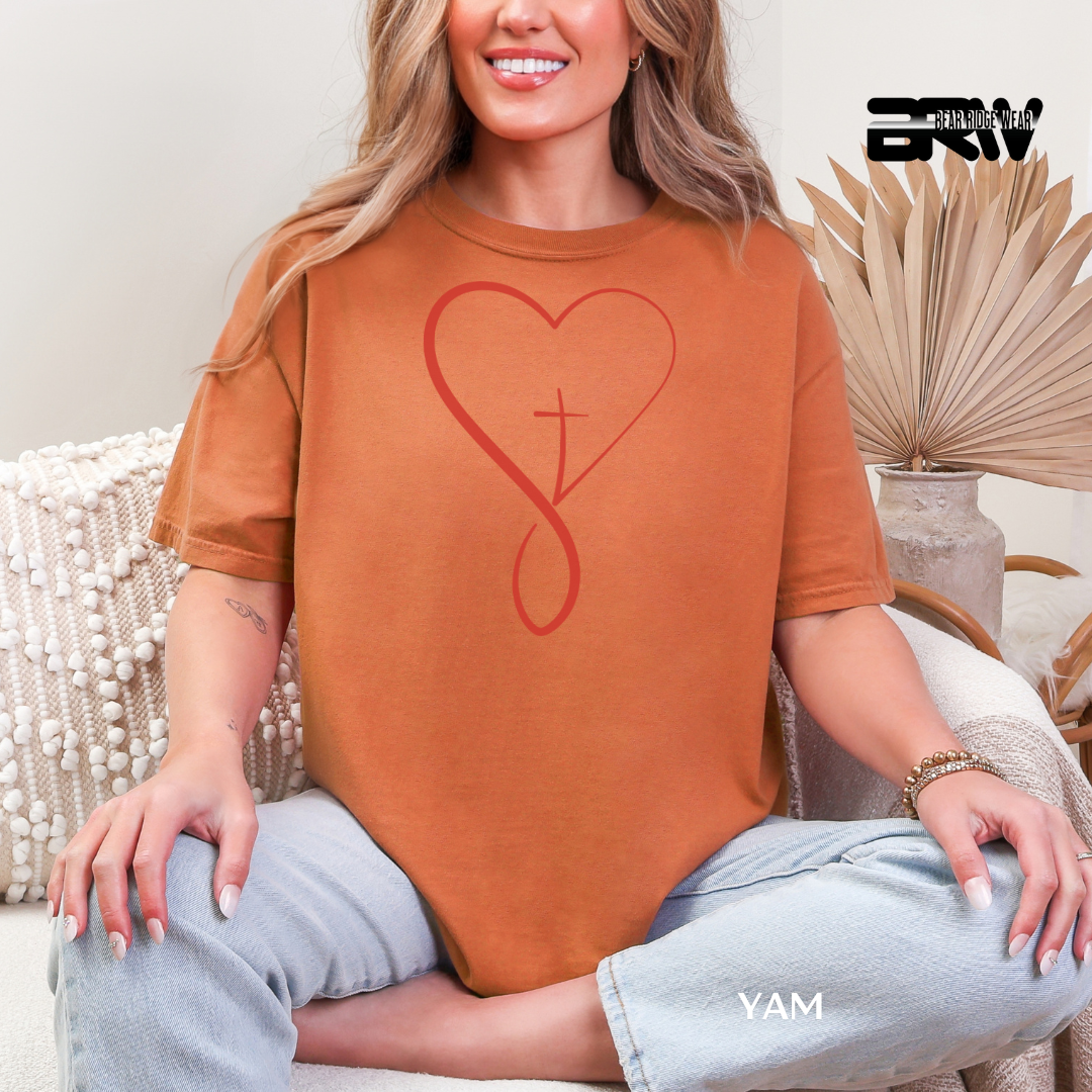 Woman wearing an orange t-shirt with a red heart and cross design, sitting on a couch.