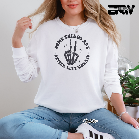 Person wearing a white sweatshirt with a graphic design and text, sitting indoors. SOME THINGS ARE BETTER LEFT UNSAID FALL AND HALLOWEEN TEE