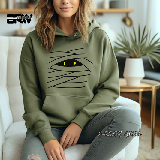 Person wearing a green hoodie with a unique design, sitting on a couch in a living room. MUMMY FALL TEE