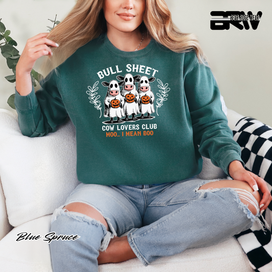 Person wearing a green sweatshirt with cow graphics and text, sitting on a couch. FALL AND PUMPKIN TEE