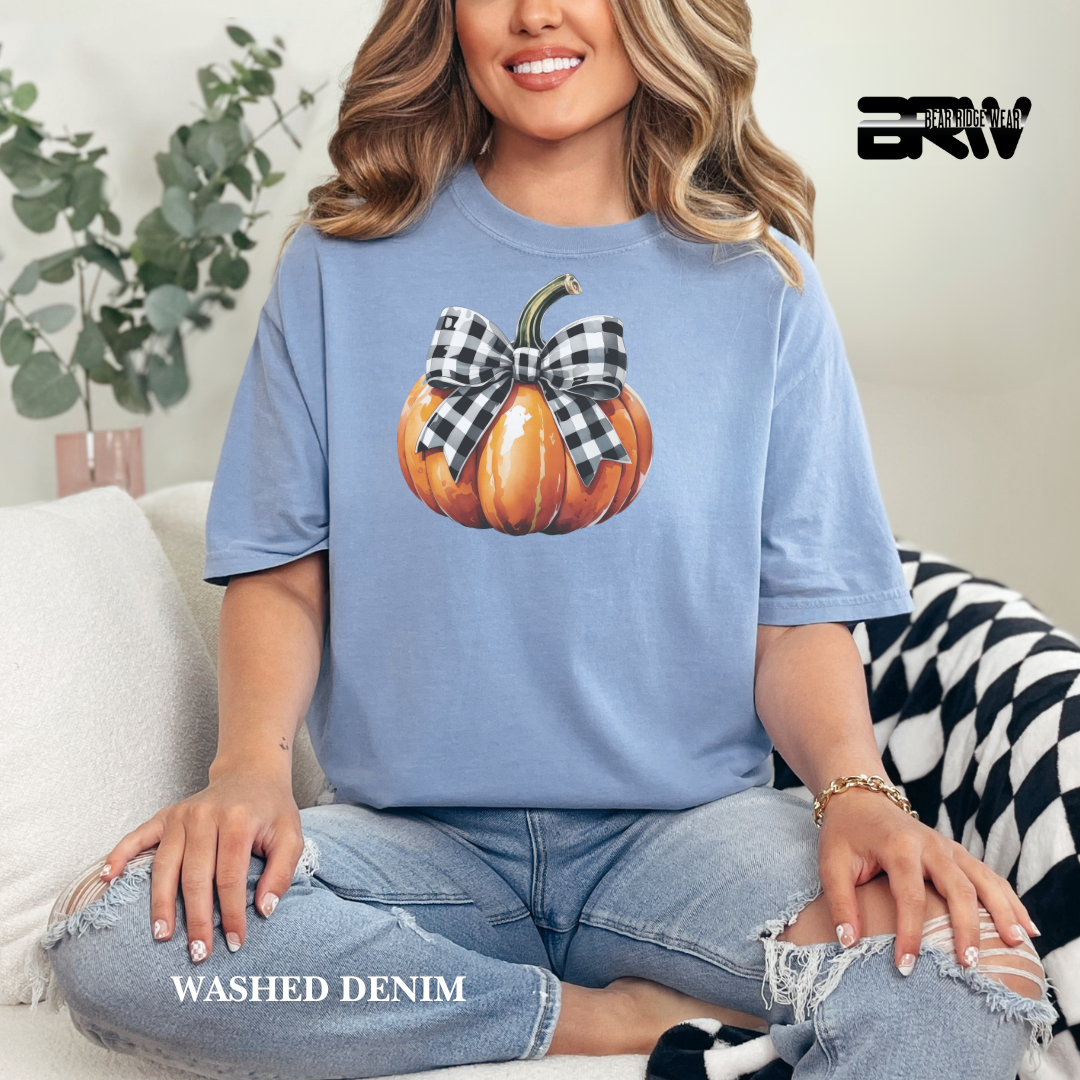 Woman wearing a blue t-shirt with a pumpkin design, sitting on a couch.
