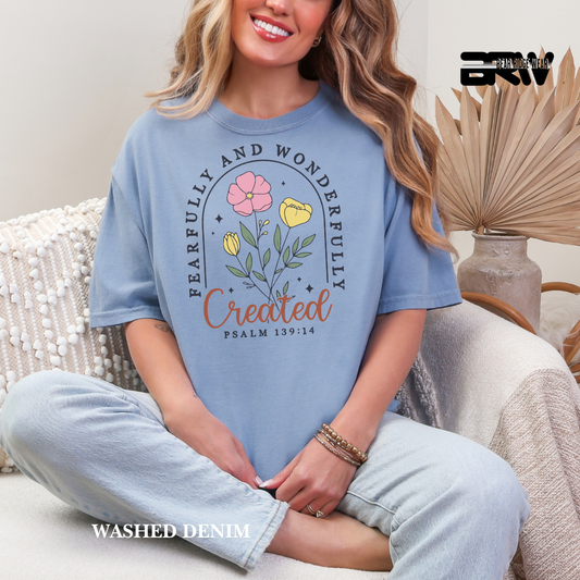 Woman wearing a blue t-shirt with floral design and text, sitting on a couch.