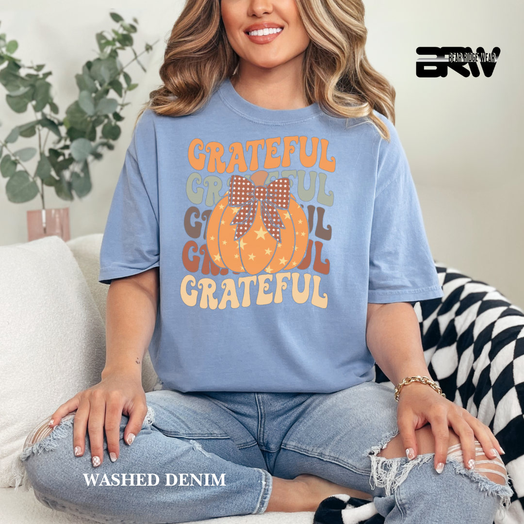 Woman wearing a blue t-shirt with 'Grateful' text and pumpkins, sitting on a couch.