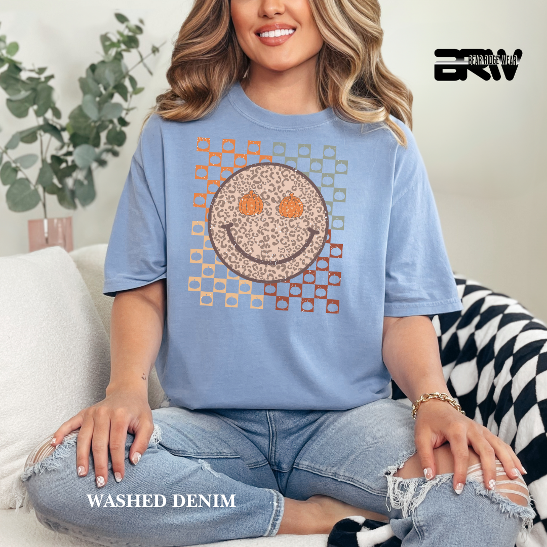 Woman wearing a blue t-shirt with a smiley face design, sitting on a couch.