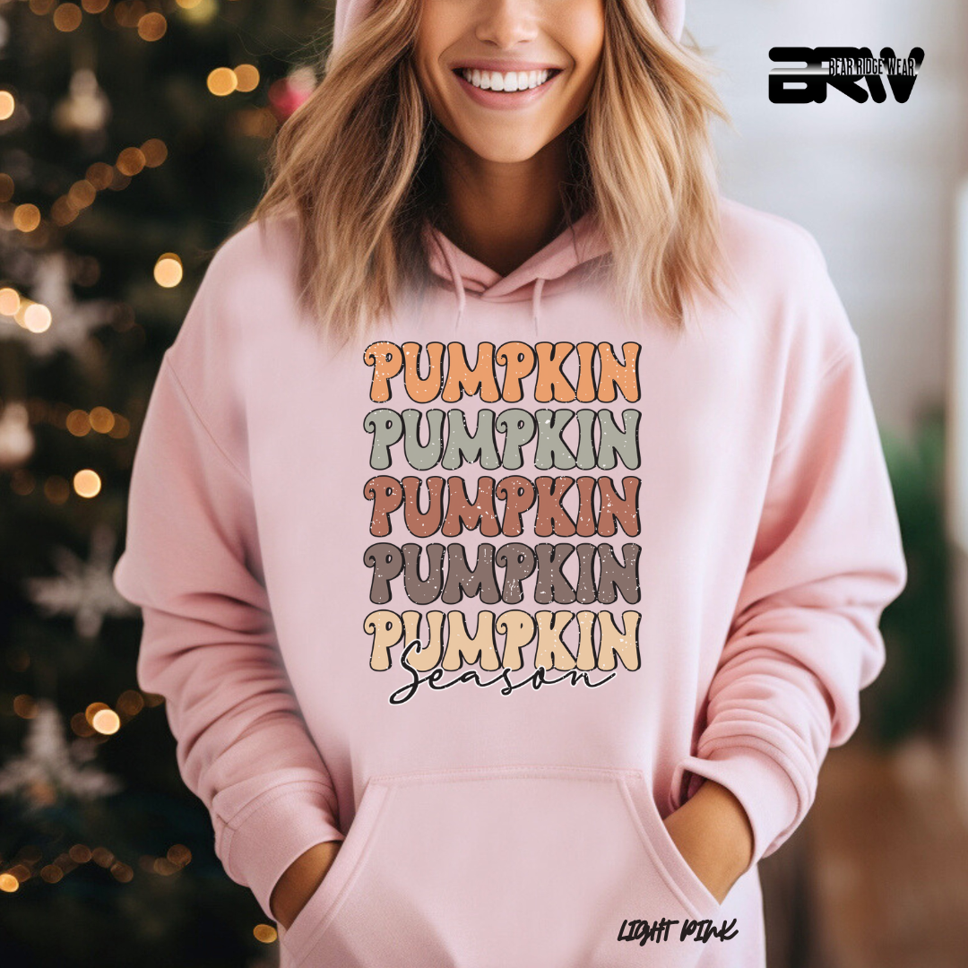 Person wearing a pink hoodie with 'Pumpkin Season' text in front of a Christmas tree.