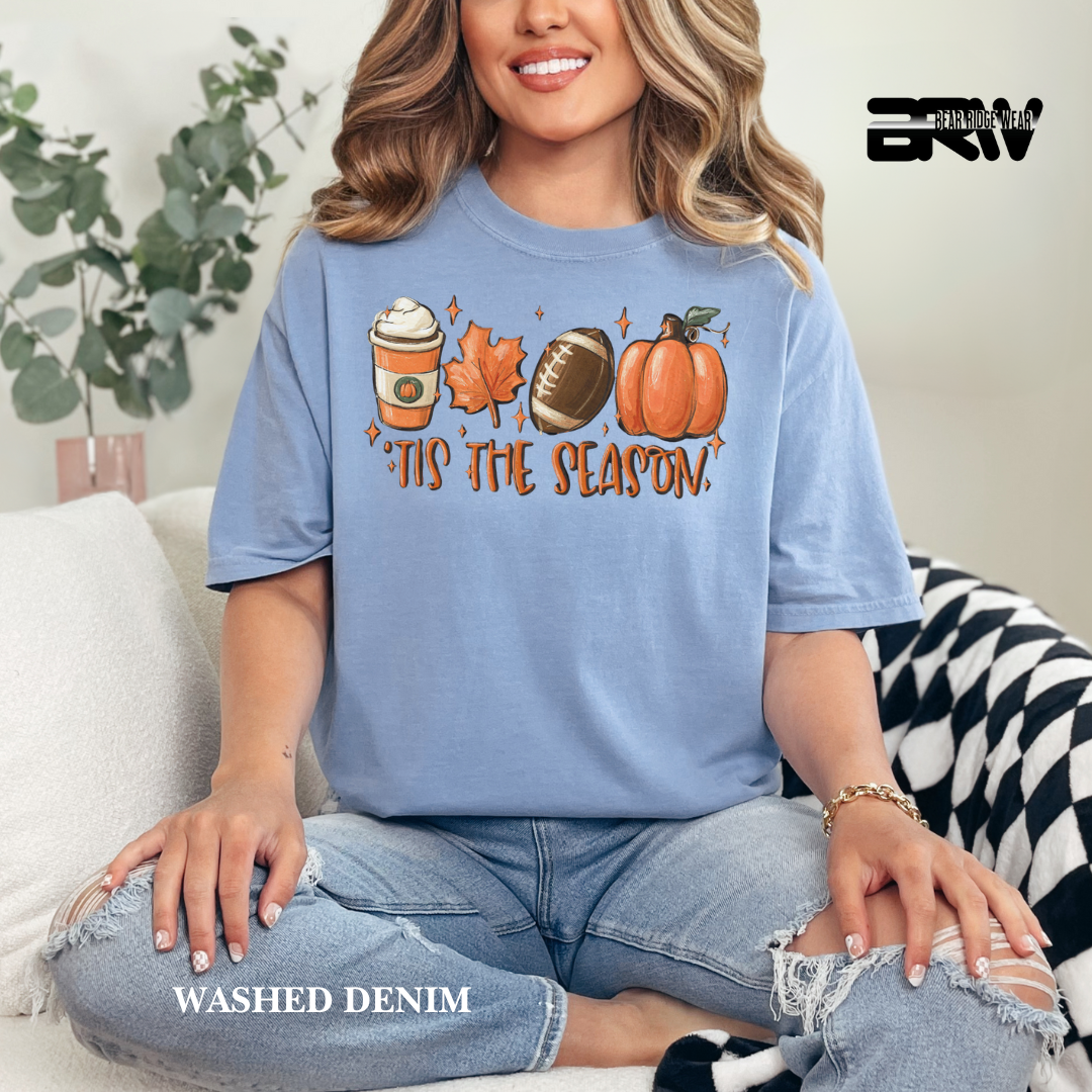 Woman wearing a blue t-shirt with autumn-themed graphics and text, sitting on a couch.