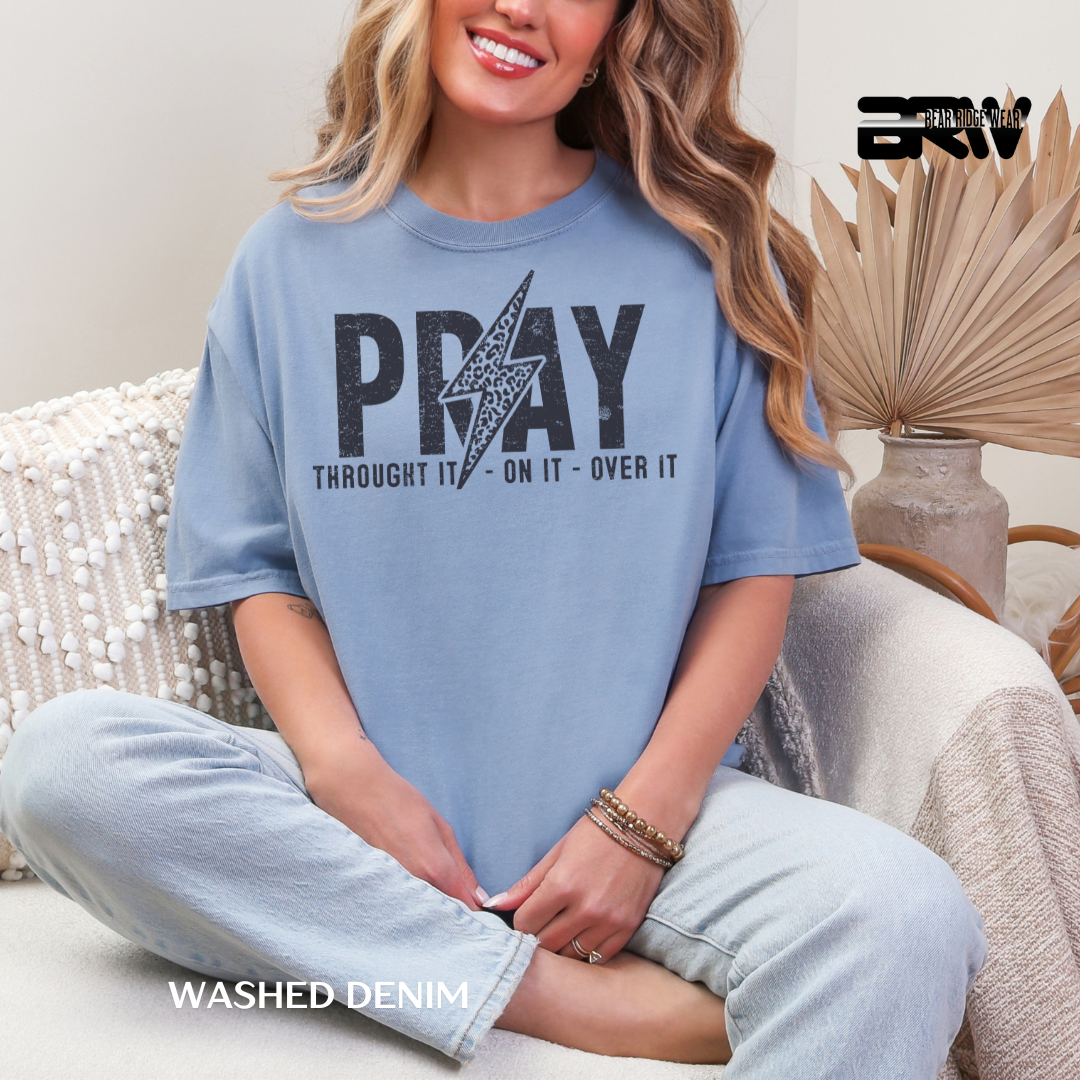 Woman wearing a blue t-shirt with 'PRAY THROUGH IT, ON IT, OVER IT' text sitting on a couch.